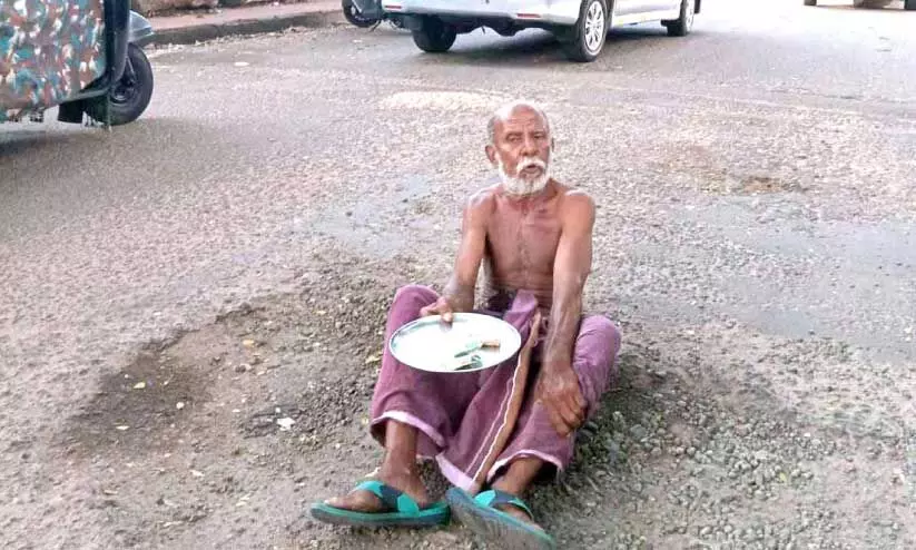 കൈവ​ണ്ടി​ത്തൊ​ഴി​ലാ​ളി ഉ​മ്മ​ർ റോ​ഡി​ലെ കു​ഴി​യി​ൽ കു​ത്തി​യി​രു​ന്ന് ഭി​ക്ഷ യാ​ചി​ച്ച് പ്ര​തി​ഷേ​ധ​സ​മ​രം ന​ട​ത്തു​ന്നു