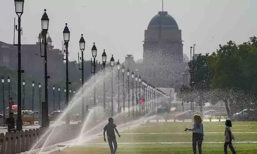 A family stands under spray to beat the heat at Central Vista Lawns near India Gate (Credits: PTI)